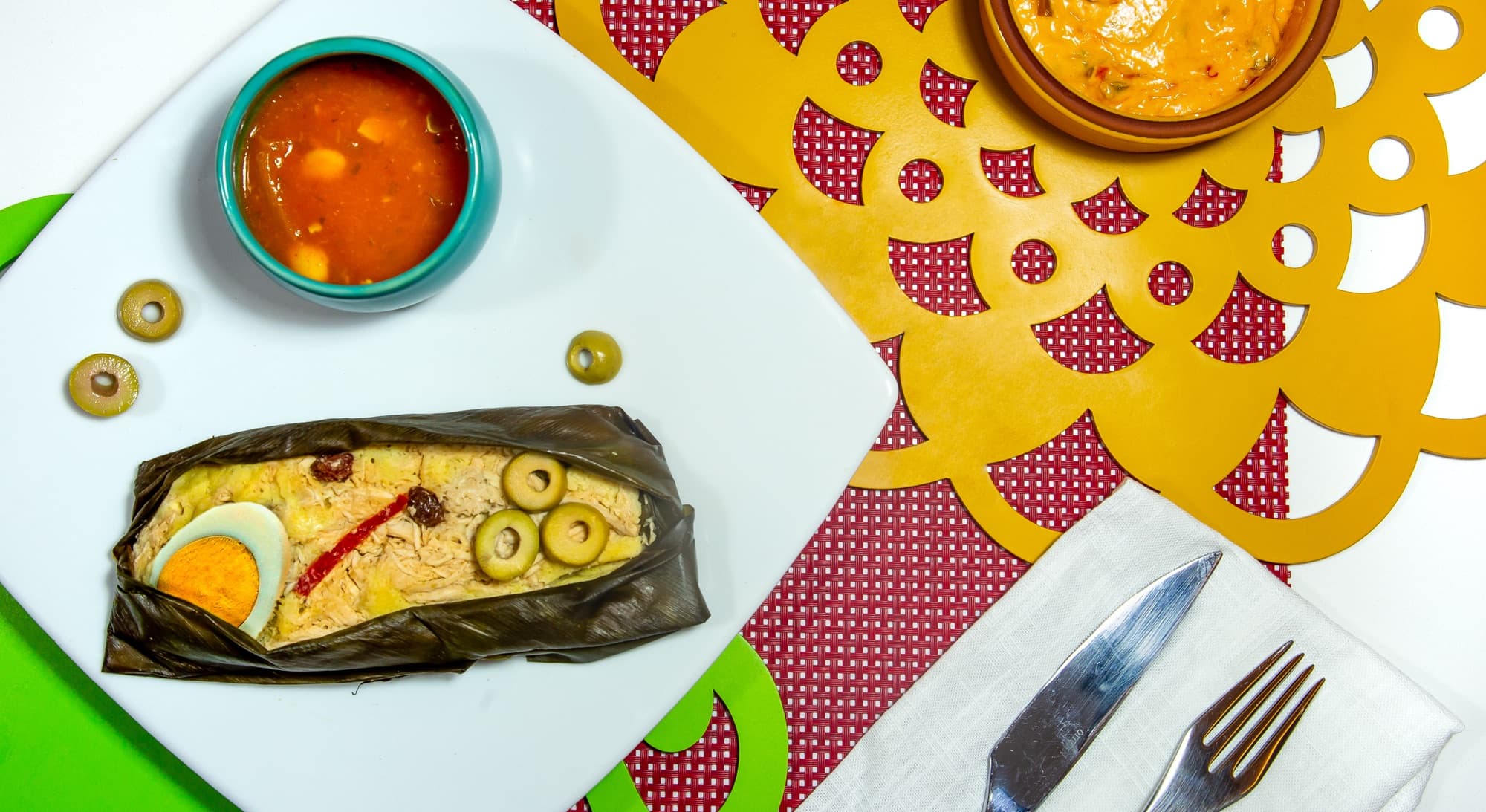 Tamal de pollo Kamimo abierto en su hoja, con huevo, aceitunas y pasas